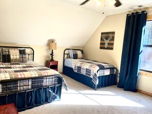 Un dormitorio con dos camas, una mesita de noche, una lámpara, un adorno de cabeza de ciervo en la pared y una ventana con cortinas.