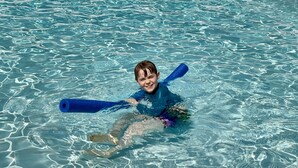 Un enfant dans une piscine, équipé de bouées bleues.