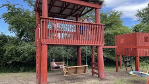 Une structure de jeu en bois rouge, avec une balançoire et un toboggan.