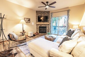 A living room with a fireplace, a ceiling fan, a television, and a view of the outdoors.