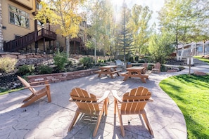 Un patio al aire libre con sillas Adirondack y mesas de picnic, rodeado por un muro de piedra y vegetación.