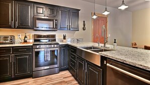 A modern kitchen with dark cabinetry, stainless steel appliances, a granite countertop, and pendant lighting.
