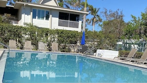 Une piscine dont le bord est recouvert de carreaux bleus, entourée de chaises longues, et une maison avec un balcon en arrière-plan.