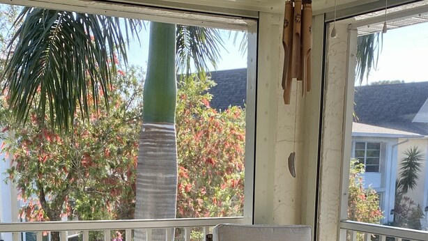 Un balcon abrité, doté de meubles en osier et offrant une vue sur un jardin.