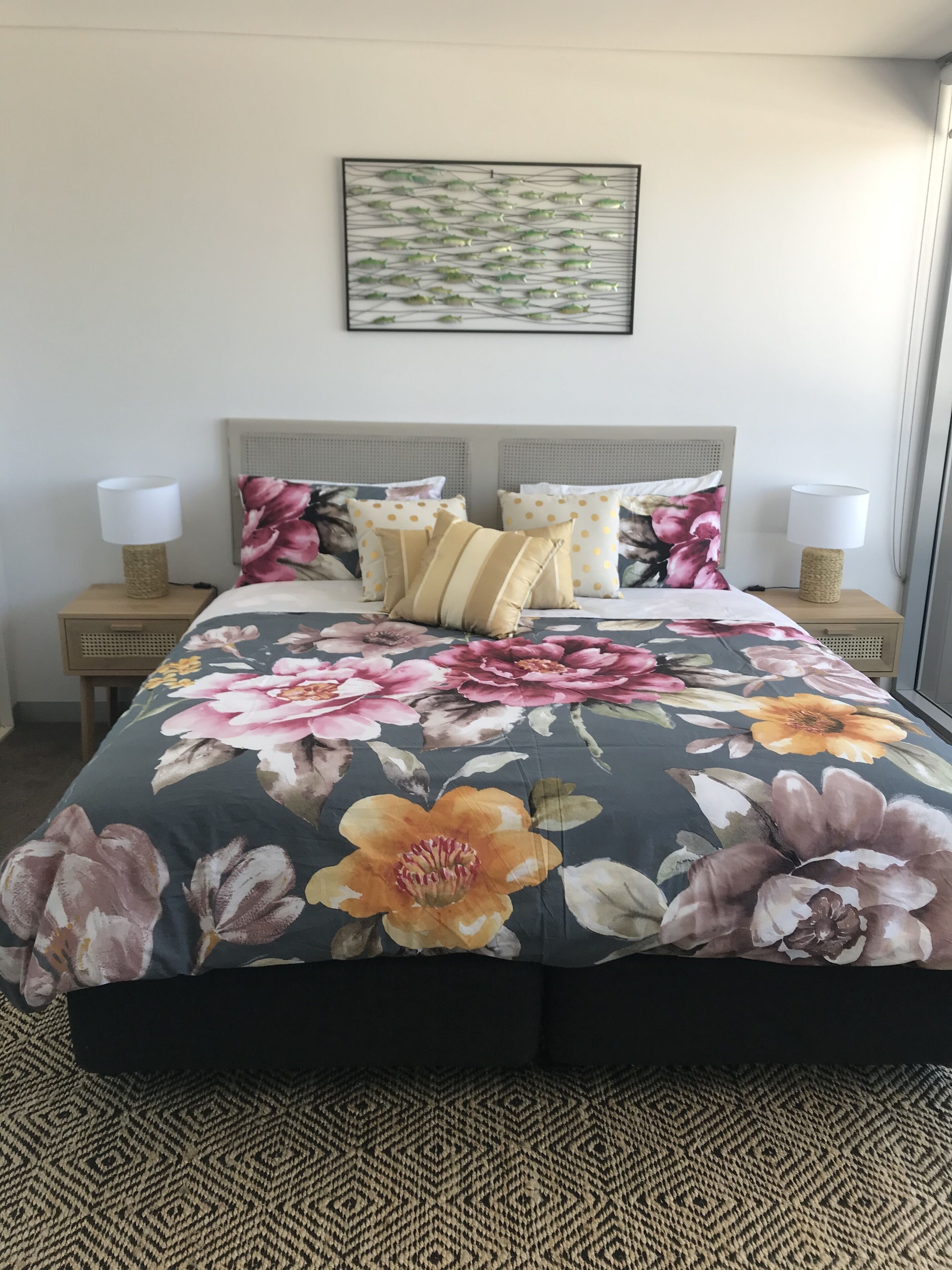 Un lit recouvert d’une couvre-lit à motifs floraux, deux tables de chevet avec des lampes et un tableau encadré accroché au mur.