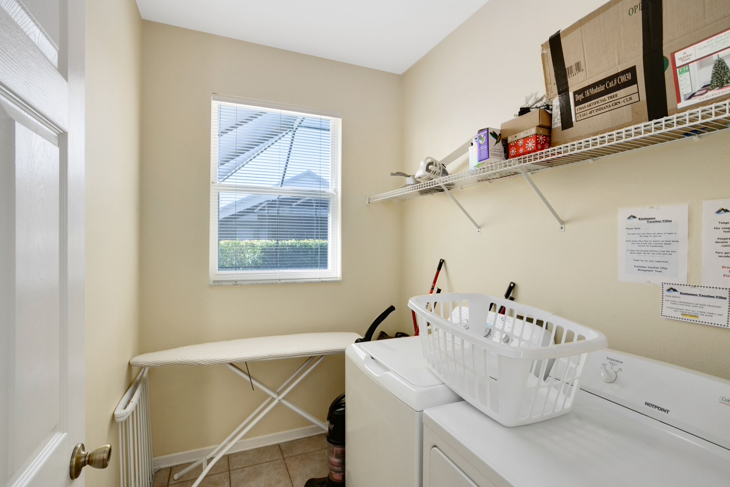 A laundry room with a drying rack, a washing machine, and a window with blinds.