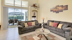 A spacious living room with two grey sofas, a glass coffee table, and a large sliding glass door leading to an outdoor patio.