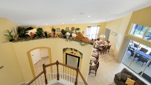 A spacious living area with a high ceiling, a dining area with a long table, and a staircase leading to an upper level.