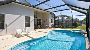 A swimming pool with a glass enclosure, lounge chairs, and a patio area with a table and chairs.