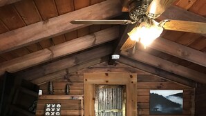 A cozy attic bedroom with a checkered bedspread, a wooden sloped ceiling, a mounted TV, and a framed picture of a bear in a forest. - Maggie Valley Cabin off the Blue Ridge Pkwy. (Maggie Valley)