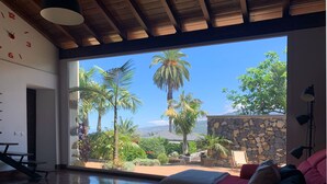 A spacious living room with a large window offering a view of a tropical garden and a stone wall. - Finca La Masía - Relax - Vistas - Internet (La Orotava)