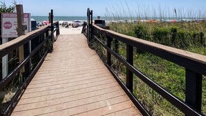 Une promenade en bois menant à une plage, avec un ciel dégagé.
