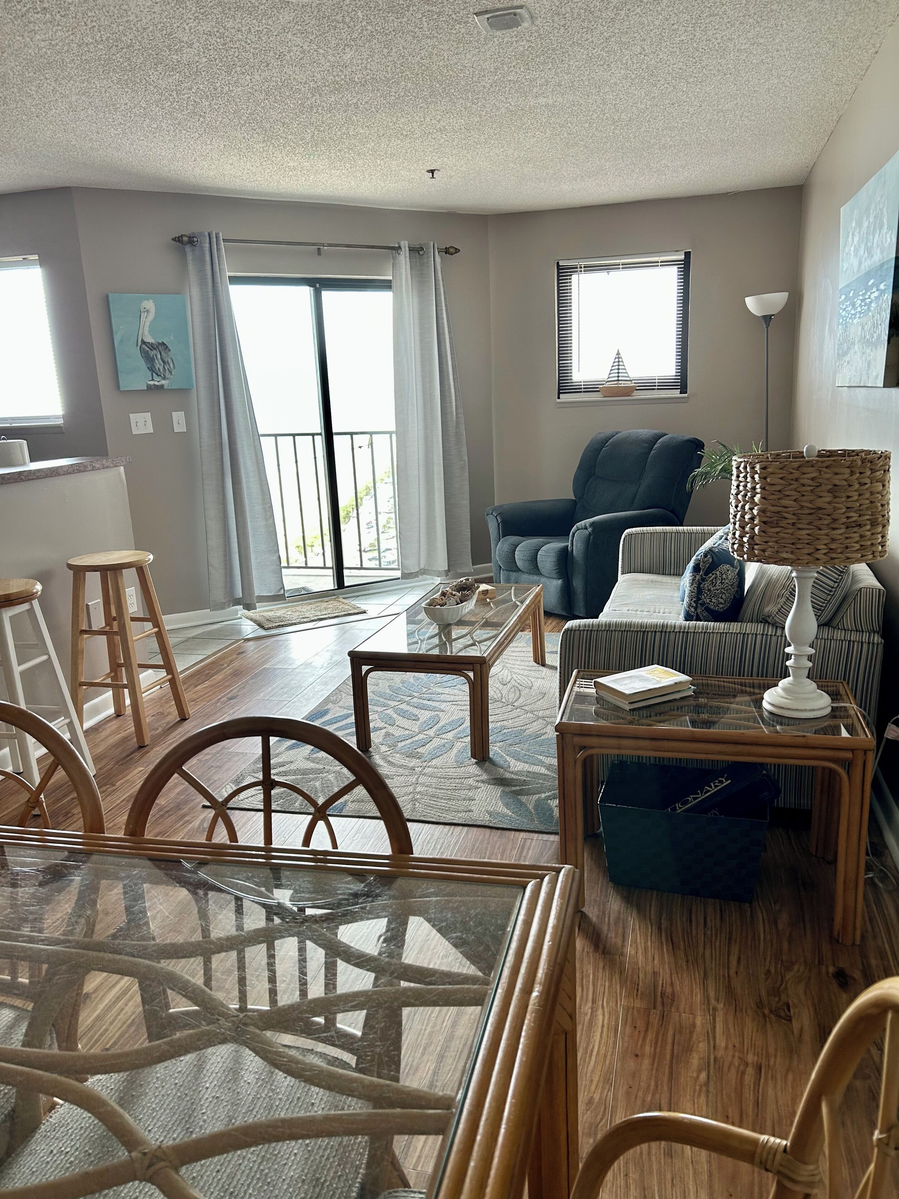 A modern living room with a glass coffee table, a sofa, a dining table with chairs, and a view of the outdoors through large windows.