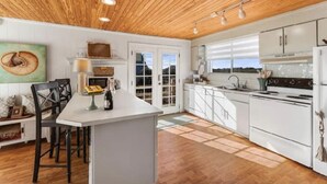 Une cuisine moderne avec des meubles blancs, un îlot central et un plafond en bois.