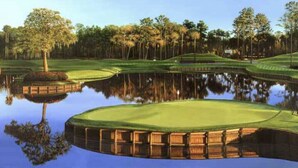 Un parcours de golf avec un étang qui reflète la verdure et les arbres, le tout entouré d’une clôture en bois.