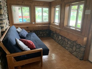 Ein gemütliches Zimmer mit einem hölzernen Bett, Steinwänden und großen Fenstern mit Blick ins Freie.