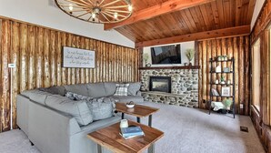 Una sala de estar acogedora con chimenea de piedra, paredes de madera y un sofá gris.
