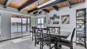 Un comedor con una mesa y sillas de madera, una estantería y vistas a un lago.