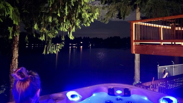 Un jacuzzi con terraza de madera y vista al lago de noche.