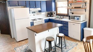Une cuisine avec des meubles de couleur bleue et blanche, un îlot central doté de tabourets, un four à micro-ondes et un évier.