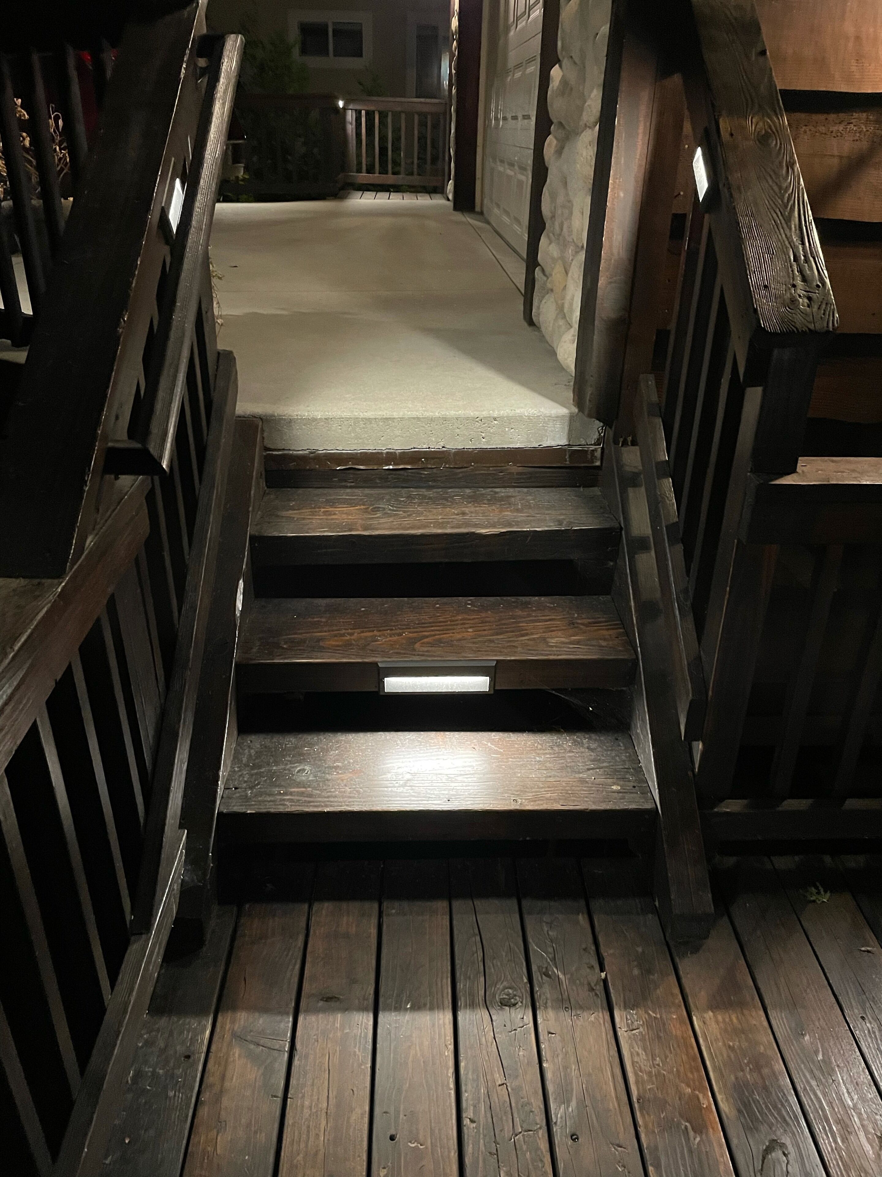 A wooden staircase leading to a covered area with a stone wall and a wooden railing.