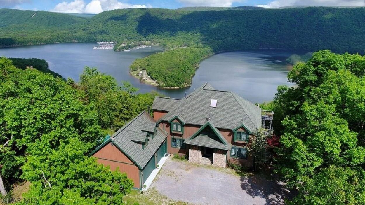 A lodge with a stone facade and green roof, surrounded by lush greenery and a lake.