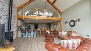 A spacious living area with a high ceiling, a fireplace, leather sofas, and a dining area with wooden furniture. - Valley View Lodge Sleeps 8 With Hot Tub (Preston)