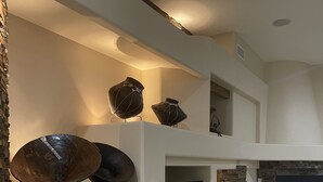A modern living room with a fireplace, built-in TV, and decorative pottery on shelves. - Legendary Desert Oasis -Heated Pool + Spa -Golf -Luxury 5BR Retreat Sleeps 12  (Phoenix)