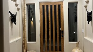 Um corredor com porta de madeira, dois chifres de touro fixados nas paredes, um tapete tecido e um vaso grande.