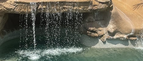 Une piscine aux eaux cristallines, agrémentée d’une cascade et entourée de rochers et de palmiers.