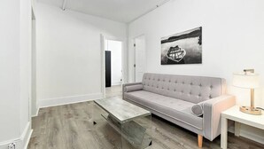 Un salon moderne avec un canapé gris, une table basse en verre et un tableau représentant un bateau sur l’eau.