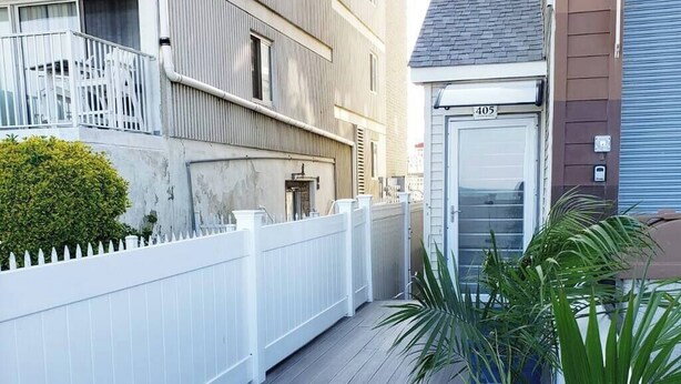 Une étroite terrasse en bois, avec une clôture blanche, un pot de fleurs et un bâtiment dont la porte de garage est marquée du numéro « 405 ».