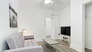 Un salon moderne avec un canapé, une table basse en verre, un téléviseur et un ventilateur de plafond.