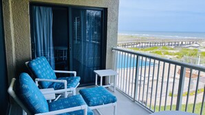 A balcony with white chairs and a small table, overlooking a pool and beach area. - Amazing Pool/Oceanfront Views from this Second Floor Condo at Amelia by the Sea! (Fernandina Beach)
