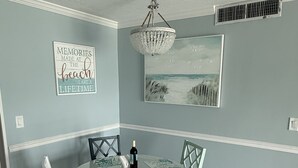 A dining area with a round table, white chairs, a chandelier, and wall art. - Dolphin & Manatee At Your Back Door!! (Treasure Island)