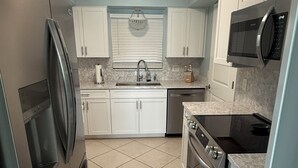 A compact kitchen with white cabinets, a stainless steel refrigerator, a microwave, and a dishwasher. - Dolphin & Manatee At Your Back Door!! (Treasure Island)