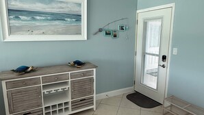 A room with a tiled floor, a white door, a framed picture of a beach, and a wooden console table with drawers. - Dolphin & Manatee At Your Back Door!! (Treasure Island)