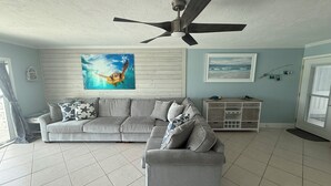 A living room with a grey sofa, a grey armchair, a ceiling fan, a wooden cabinet, and a framed picture of a sea turtle. - Dolphin & Manatee At Your Back Door!! (Treasure Island)