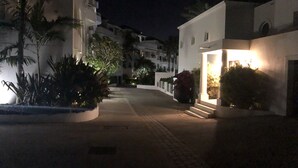 Une vue nocturne d’une rue, avec des bâtiments, des palmiers et une entrée illuminée.