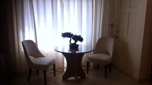 Un coin repas avec une table ronde et deux chaises, une plante en pot posée sur la table, et une porte visible au fond.