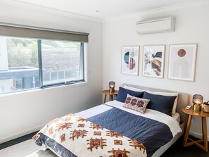 A bedroom with a bed, a window, a wall-mounted air conditioner, and framed artwork. - Beautiful Martha Cove home - 100m from water (Safety Beach)