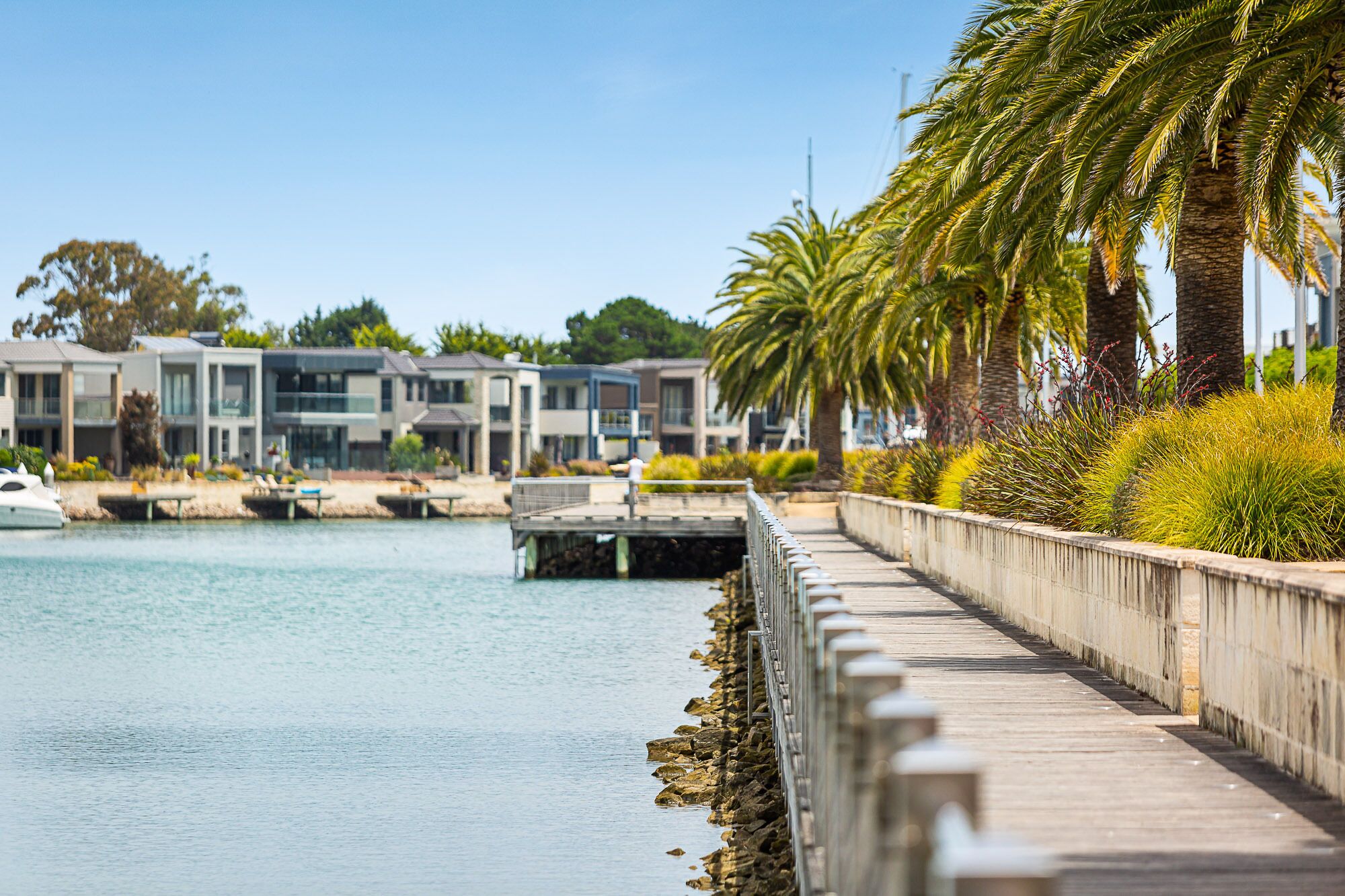A waterfront promenade with modern buildings, a dock, and a wooden walkway.