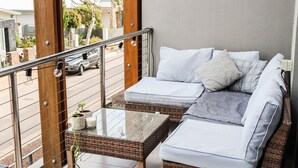 Ein Balkon mit Korbmöbeln, einem Glastisch und Blick auf die Straße.