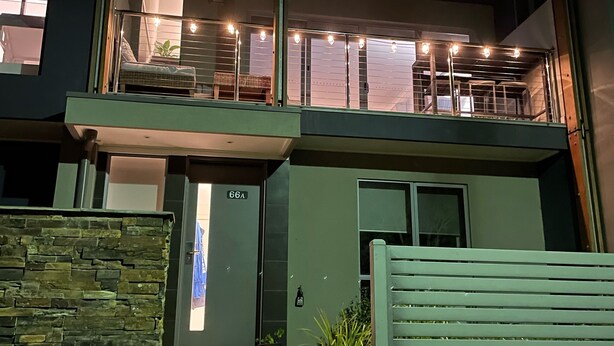 Ein modernes, zweistöckiges Gebäude mit Steinverkleidung, einem Balkon mit Lichterketten und freiem Blick auf den Eingang.