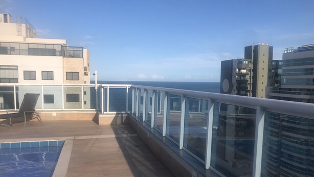 Un balcon avec une piscine, des garde-corps en verre et une vue sur l’océan et les bâtiments.
