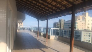 Un balcon couvert, doté d’un sol carrelé et de rampes en métal, qui offre une vue sur un paysage urbain avec des bâtiments modernes.