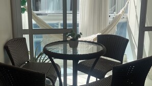 Un balcon avec une table en verre et quatre chaises en osier, un rideau blanc et un hamac.