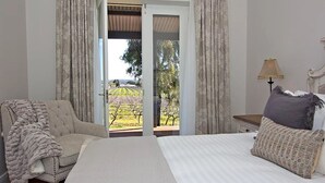 Un dormitorio con una cama grande, una silla y vistas a un viñedo a través de un ventanal corredera.
