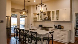 Una cocina moderna con armarios blancos, una isla central con taburetes de bar, una estufa de acero inoxidable e iluminación colgante.