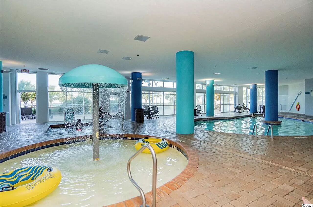 Zona de piscina interior con fuente de agua, un flotador amarillo inflable y un tobogán de agua azul.